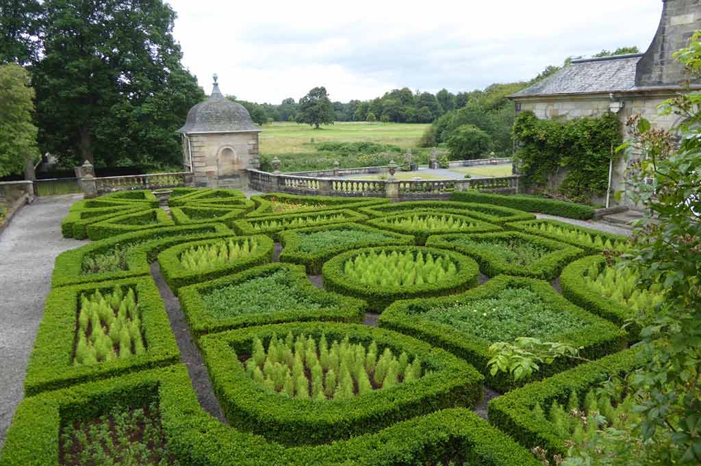 A manicured hedge maze in front of the stone garden pavilion at Pollok Country Park