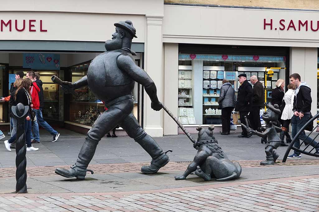 A bronze statue of a man walking a dog on a busy Dundee street