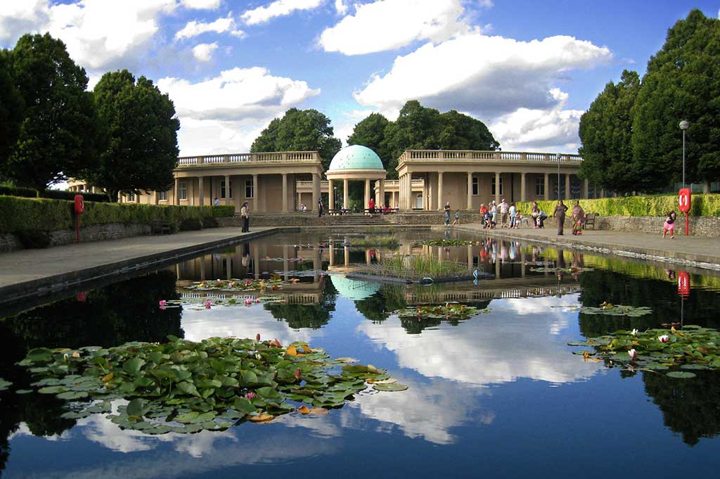 A pavillion at Eaton Park is reflected in the glassy surface of a lake with lilypads
