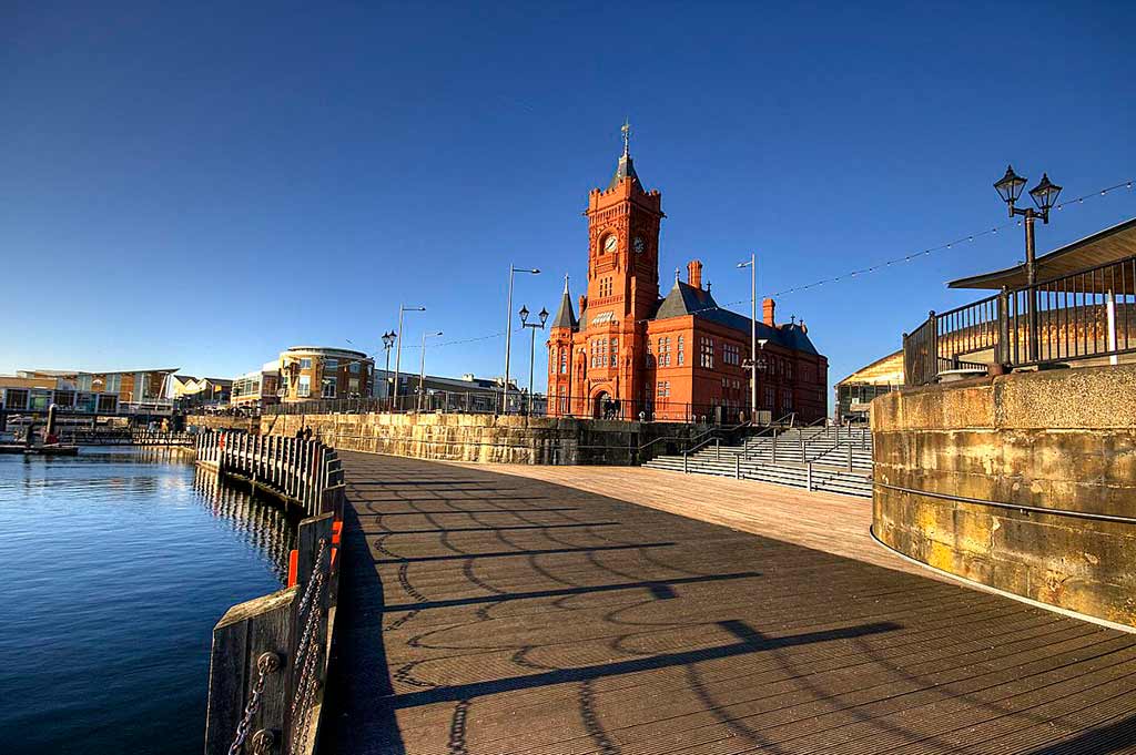 A wide shot of Cardiff Bay, with a church and a walkway on one side and blue water on the other