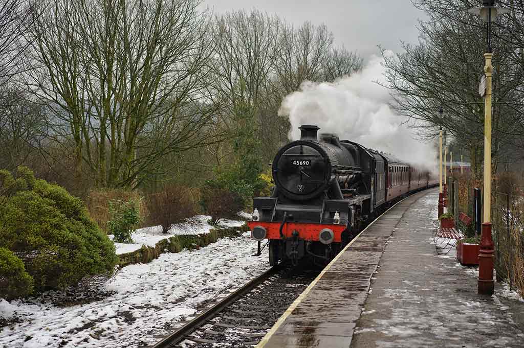 An old-fashioned, black and red steam train pulls into a station on the East Lancashire Railway line