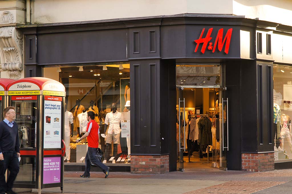 Shoppers pass by a building with a black facade and the H_M logo in red