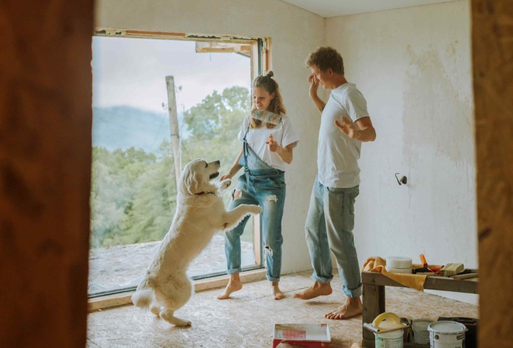 A Happy Couple Dancing With Their Dog in a room they are decorating
