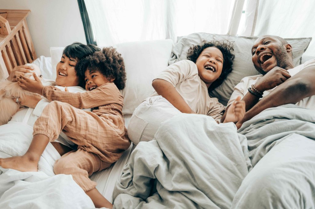 Happy multiracial family having fun together in bed with their little dog