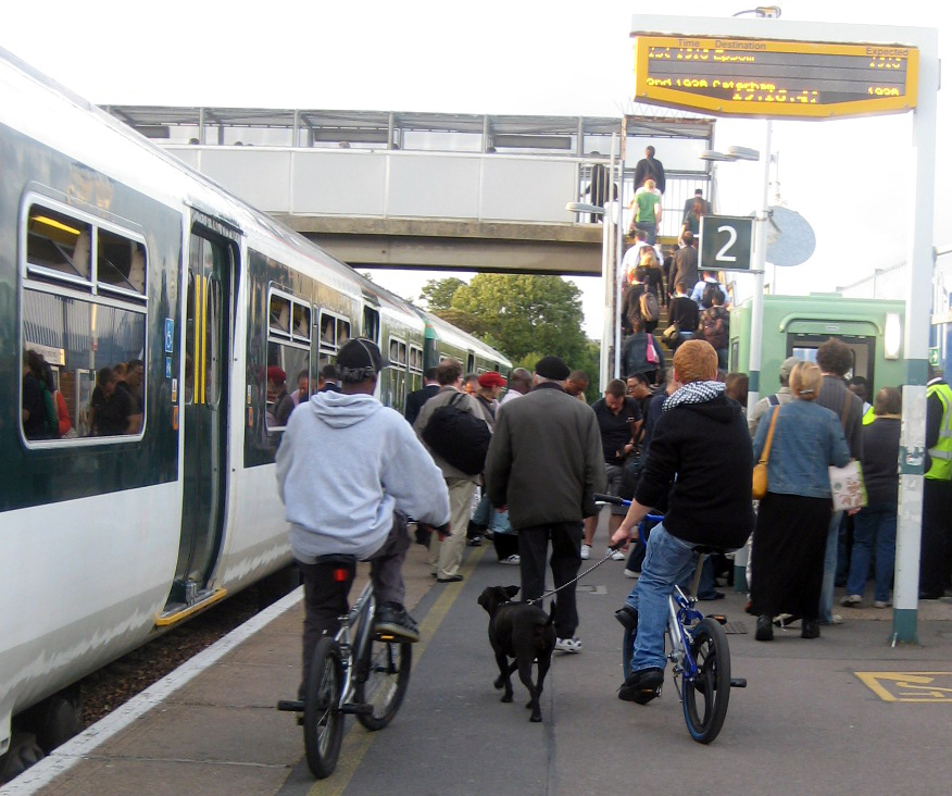 people getting off a train including two teenage boys on bikes and one has a black dog on a lead